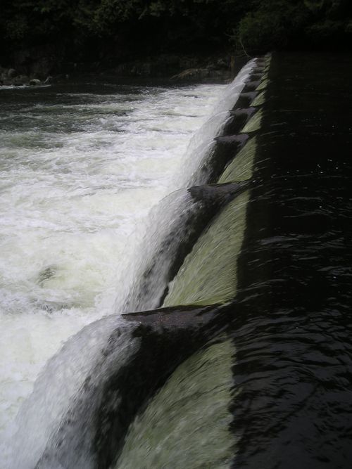 A close up of a waterfall with a river in the background.
