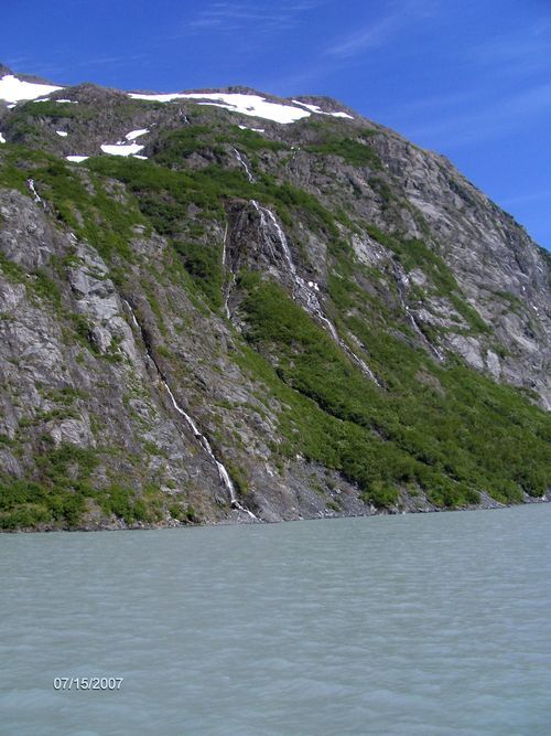 A waterfall is coming down the side of a mountain next to a lake.