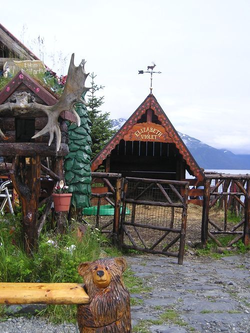 A wooden bear statue sits on a bench in front of a wooden building that says ' lodge ' on it
