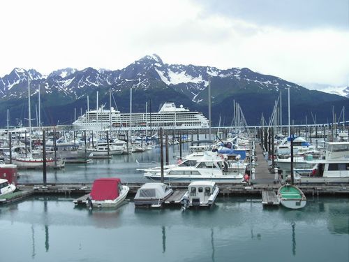 A large cruise ship is docked in a marina with mountains in the background