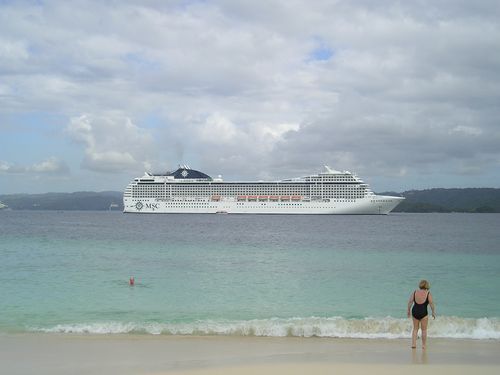 A woman standing on a beach with a cruise ship in the background