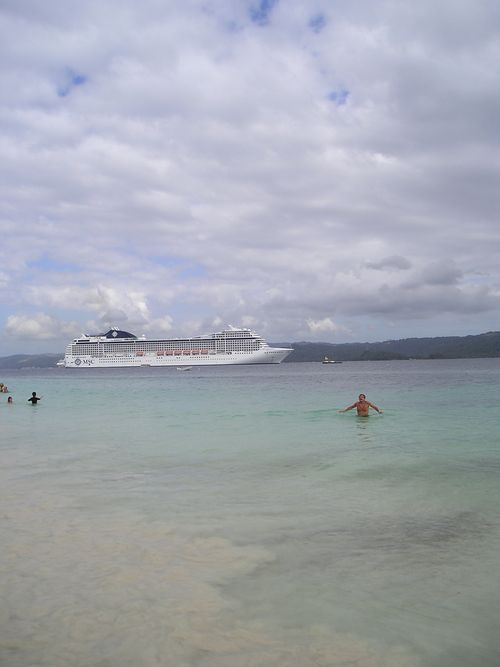 A man is swimming in the ocean with a cruise ship in the background