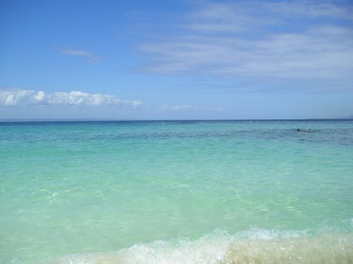A turquoise ocean with waves crashing on the beach on a sunny day.