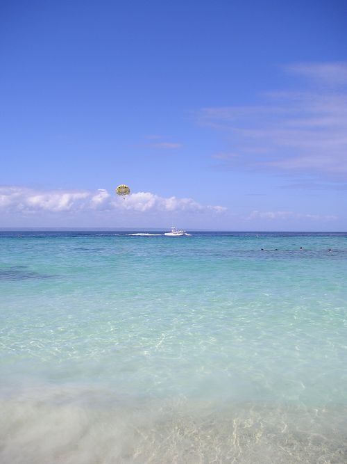 A parachute is flying over the ocean on a sunny day.