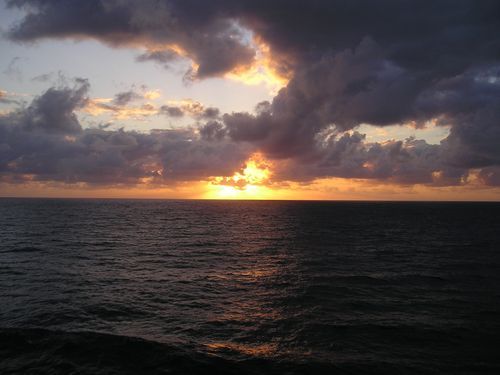 The sun is setting over the ocean with clouds in the sky