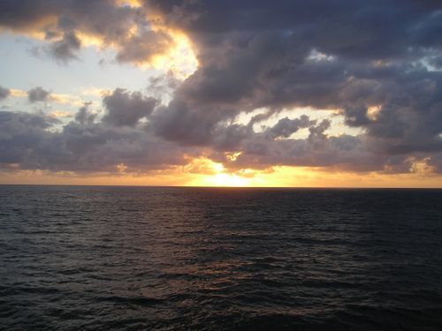 The sun is setting over the ocean with clouds in the sky