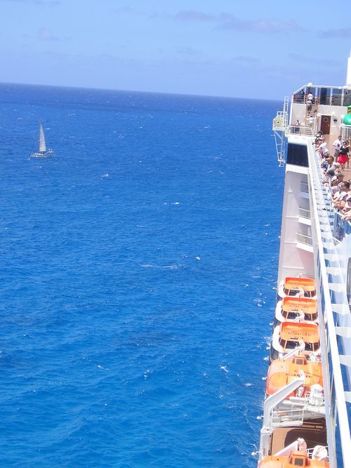 A cruise ship in the ocean with a sailboat in the distance