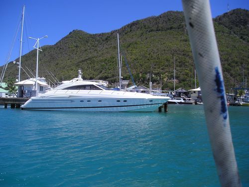 A large white yacht is docked in a harbor with mountains in the background.
