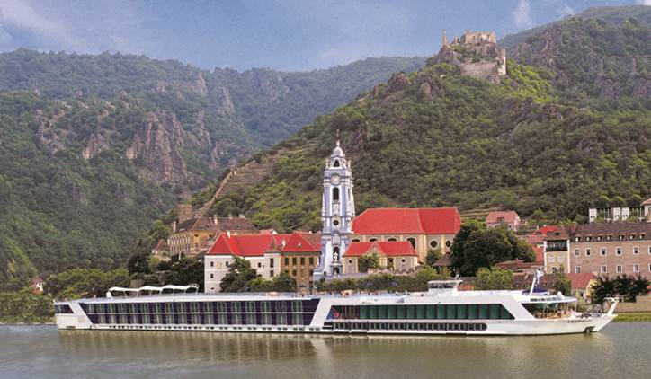 A large cruise ship is floating on a river in front of a mountain.