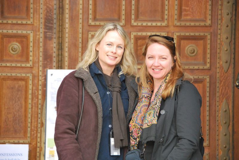 Two women are posing for a picture in front of a wooden door