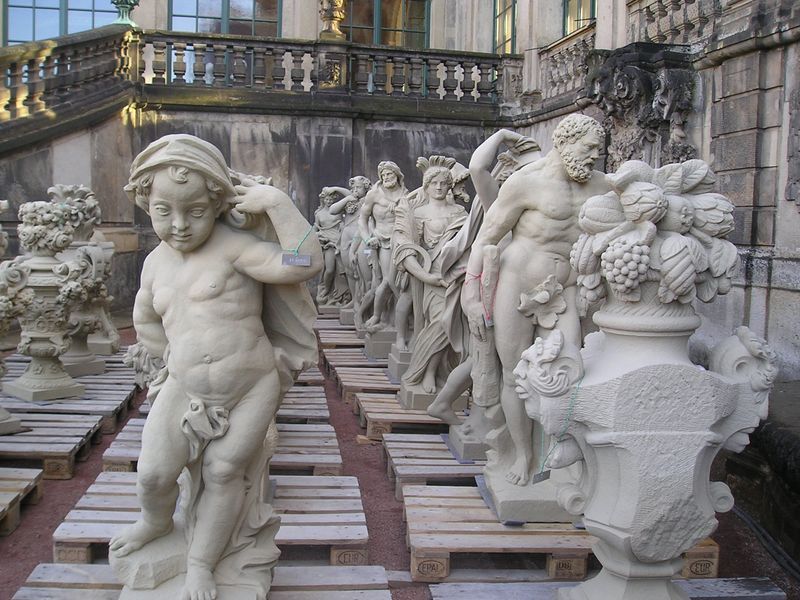 A row of statues are sitting on wooden pallets outside of a building