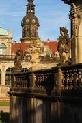 A balcony with statues and a clock tower in the background.