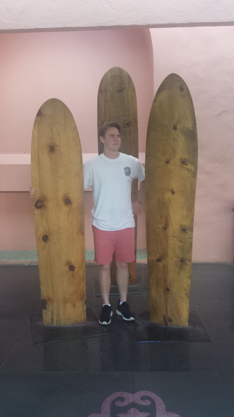 A man is standing in front of three wooden surfboards.