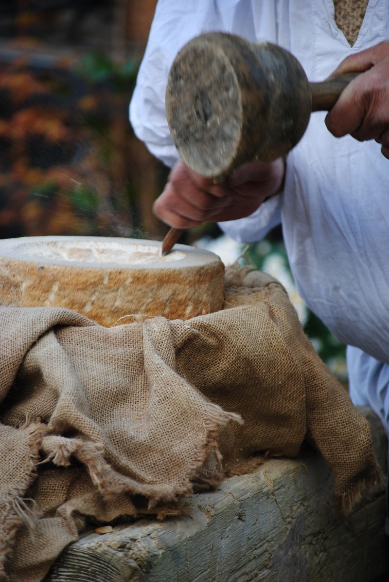 A person is holding a hammer over a piece of cheese.
