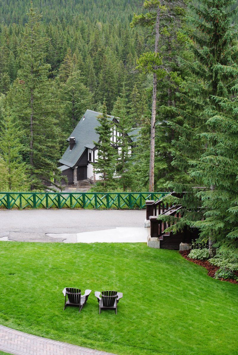 Two chairs are sitting on a lush green lawn in front of a house surrounded by trees.