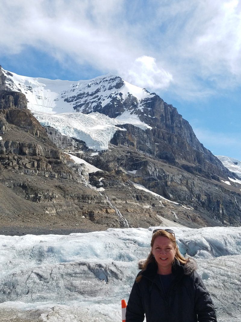 A woman is standing in front of a snowy mountain.