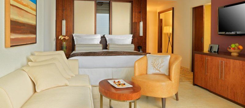 A hotel room with a couch , chair , table and television.