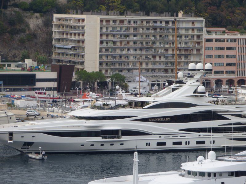 A large yacht is docked in a harbor with buildings in the background