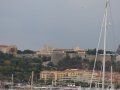 A group of sailboats are docked in a harbor with a city in the background.