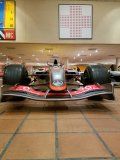 A red and black race car is parked on a tiled floor in a building.
