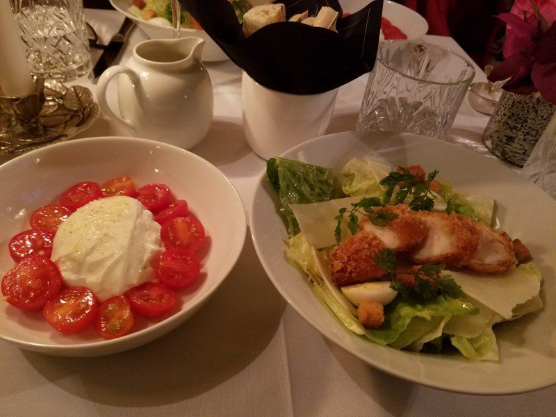 Two plates of food on a table including a salad and a bowl of tomatoes