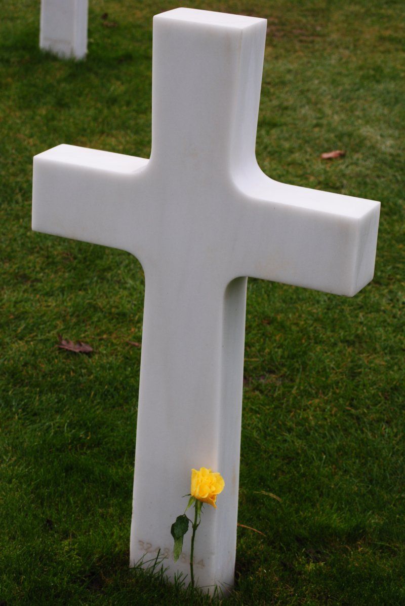 A white cross with a yellow rose in the grass
