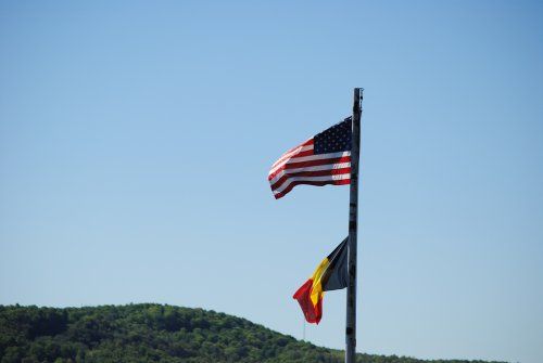 An american flag and a belgian flag are flying on a pole.