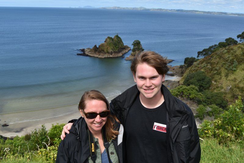 A man and a woman are posing for a picture in front of a body of water.