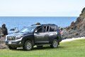 A suv is parked in a grassy field next to the ocean.