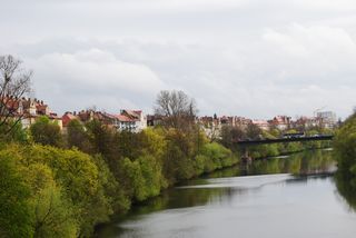 A river surrounded by trees and houses with a bridge in the background.