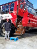 A man is standing in front of a red bus with stairs.