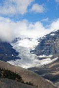 A mountain covered in snow and clouds on a sunny day.