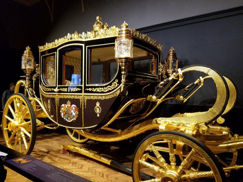 A black and gold horse drawn carriage is on display in a museum.