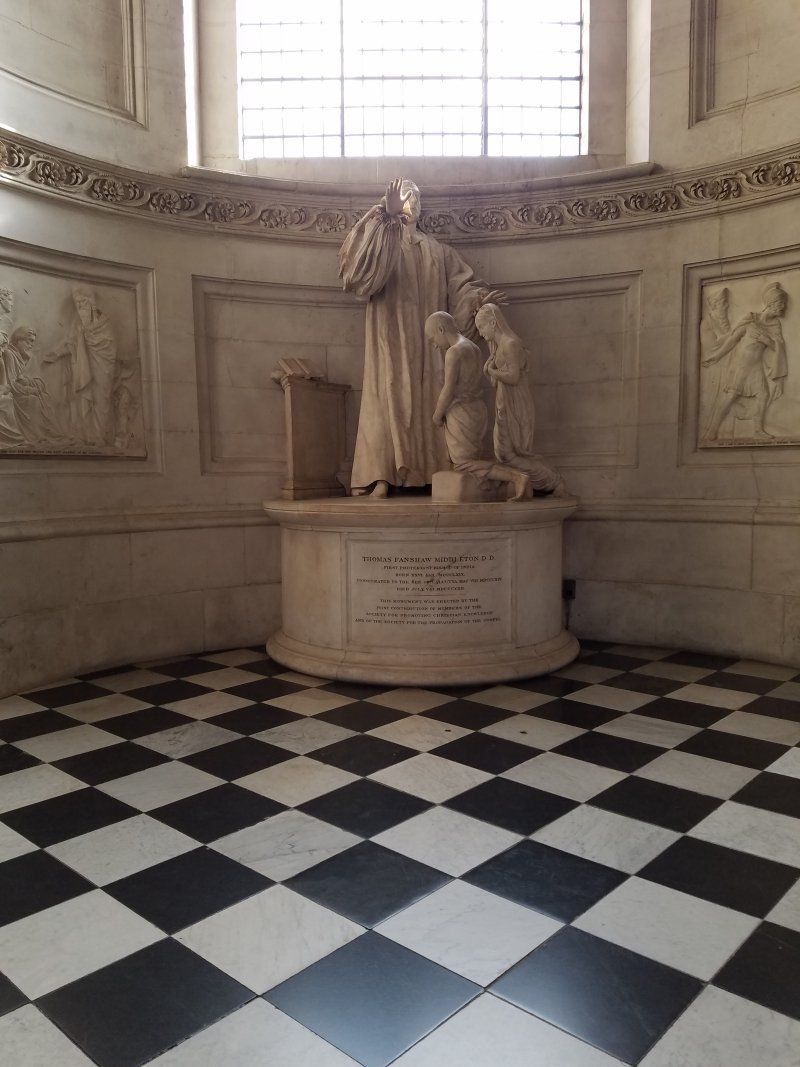 A statue of a man holding a child in a room with a checkered floor.