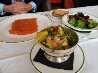 A bowl of shrimp sits on a plate next to a plate of smoked salmon