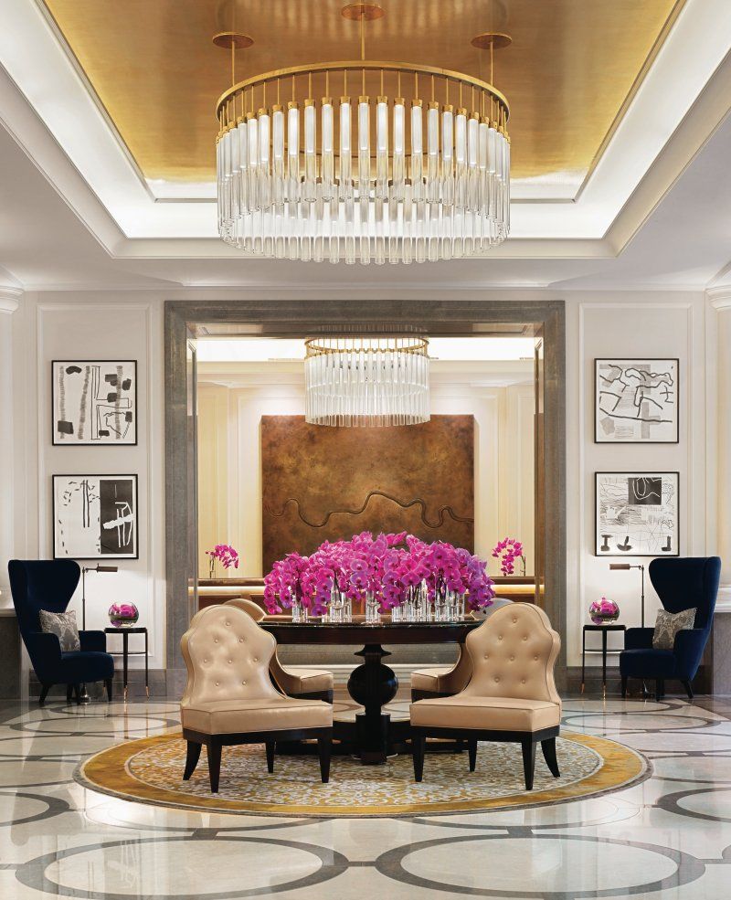 A lobby with chairs , a table and a chandelier.