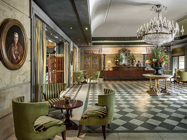 A lobby of a hotel with a checkered floor , chairs , tables and a chandelier.