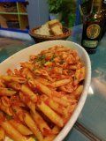A bowl of pasta with tomato sauce is sitting on a table next to a bottle of wine.