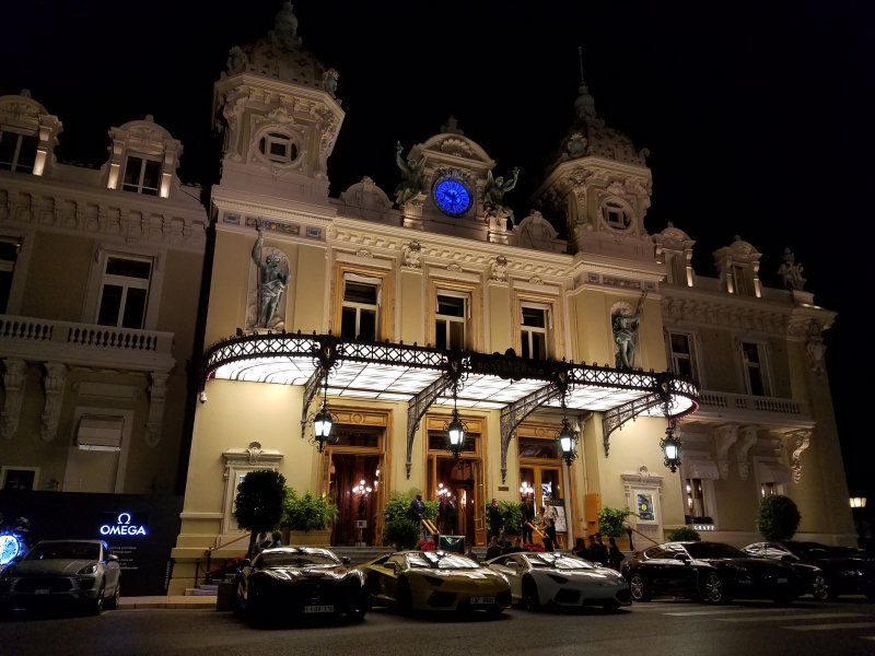 A group of cars are parked in front of a large building at night.