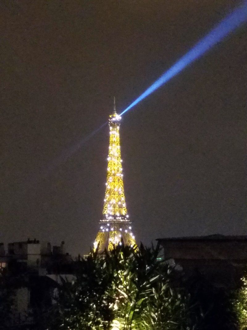 The eiffel tower is lit up at night with a blue light coming from the top