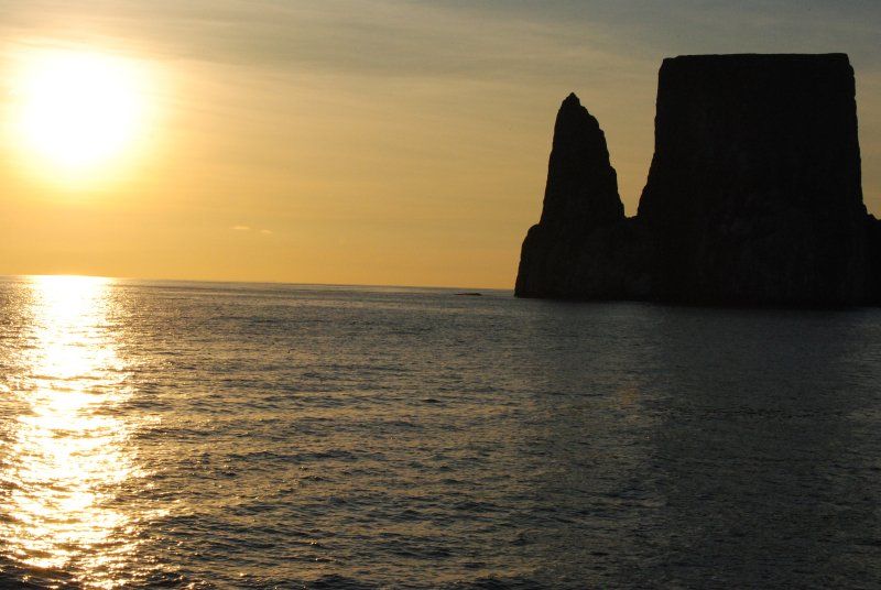 A large rock formation in the middle of the ocean at sunset