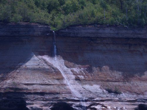 A waterfall is coming down a cliff in the middle of a forest.