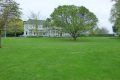 A large lush green field with trees and a house in the background.