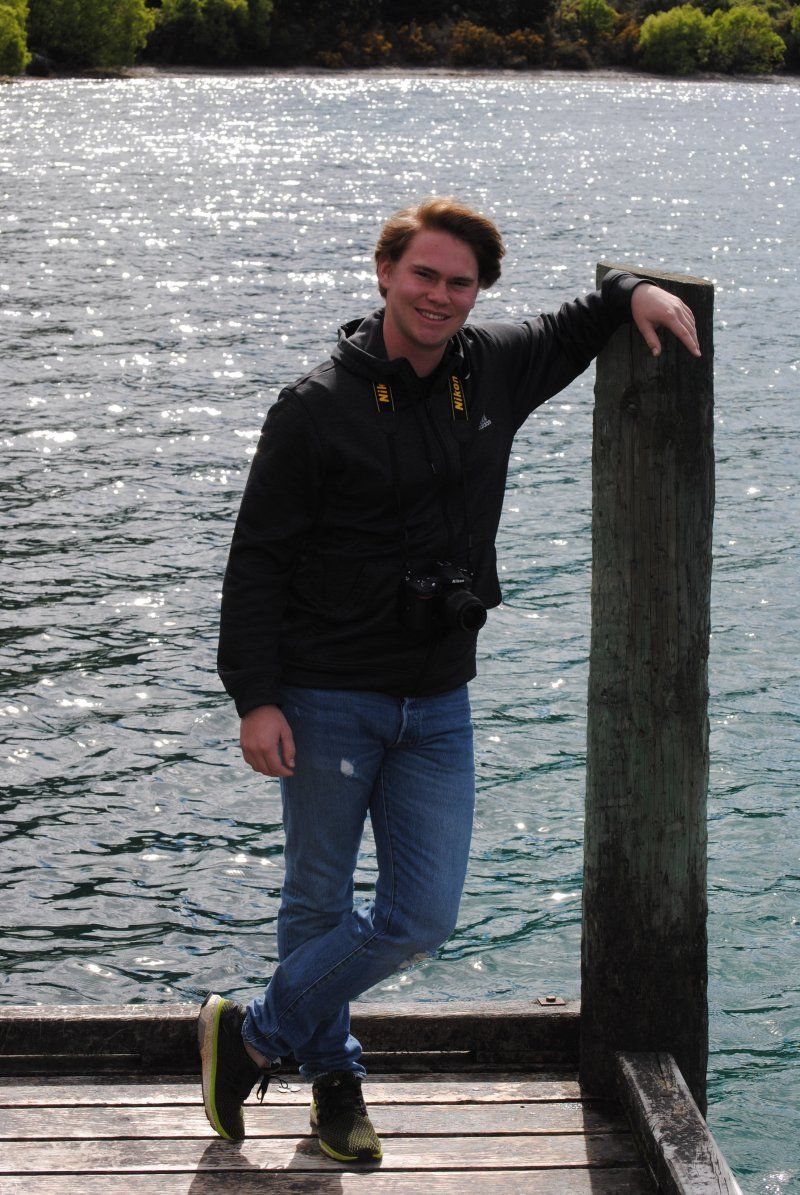A man leaning against a wooden post next to a body of water