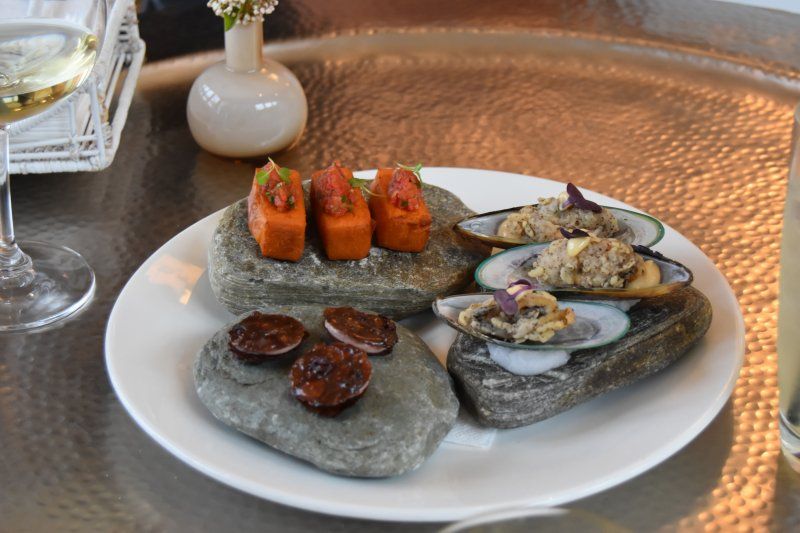 A plate of food on rocks on a table next to a glass of wine.