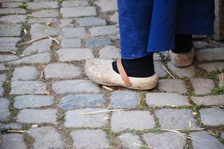 A person wearing a pair of clogs is standing on a cobblestone street.