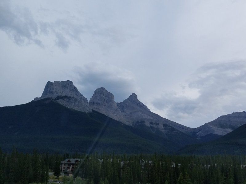 A mountain range with trees in the foreground and a cloudy sky in the background