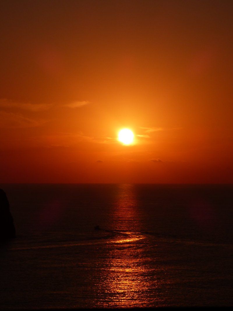 The sun is setting over the ocean with a boat in the distance.