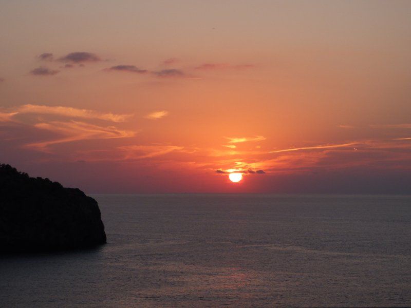A sunset over the ocean with a cliff in the foreground