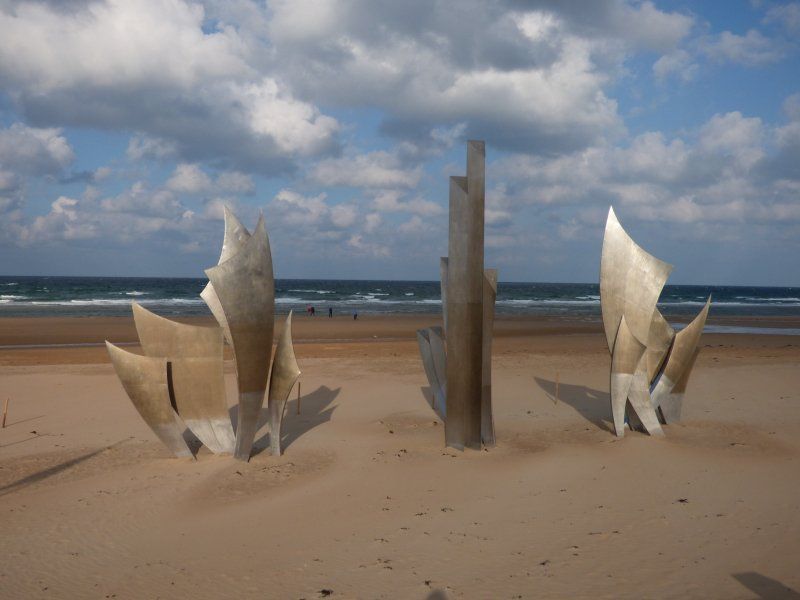 Three sculptures on a sandy beach with the ocean in the background